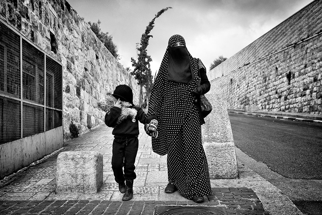 A woman and a child walking along a path beside a wall.